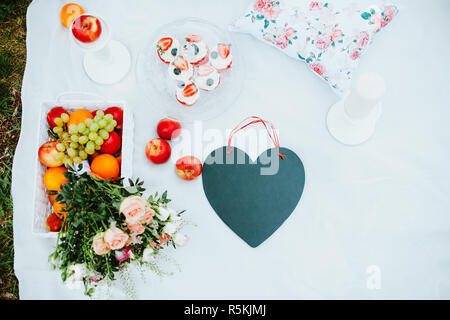 Picknick auf der Lichtung für Liebhaber mit Obst und Kuchen, schwarze Tafel in Form eines Herzens, eine Liebesgeschichte Stockfoto