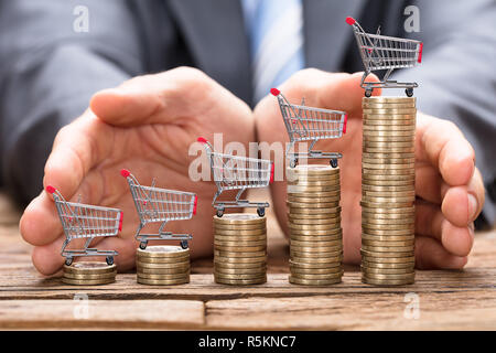 Geschäftsmann Schutz Shopping Carts auf Gestapelte Münzen Stockfoto