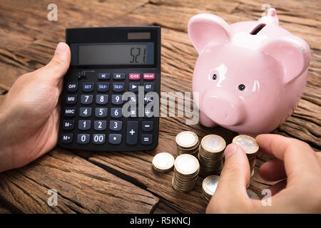 Geschäftsmann mit Rechner von Münzen und Sparschwein auf Tisch Stockfoto