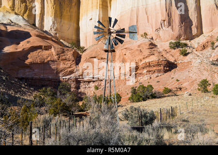 Old Ranch Windmühle und Zaun vor der bunten hohen Klippen in der Wüste Landschaft des nördlichen New Mexico Stockfoto