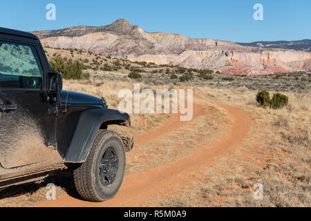 Muddy Fahrzeug mit Allradantrieb auf geschwungene Schmutz der Straße in Richtung zu einer bunten High Desert peak in der Ghost Ranch in der Nähe von Santa Fe, New Mexico Stockfoto