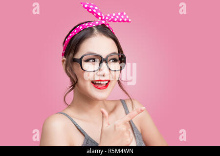 Portrait von asiatischen Mädchen mit hübsch Lächeln in pinup Style zeigt auf rosa Hintergrund Stockfoto