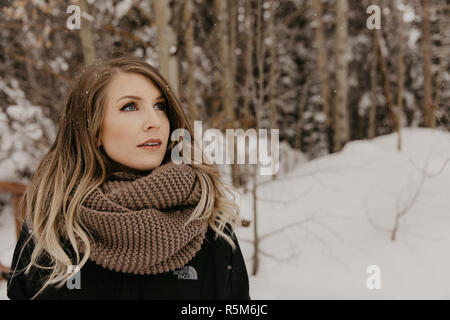 Ziemlich nette junge Erwachsene Frau blond Modell tragen Winter Mantel und Moderne Mode Schal außerhalb im kühlen Colorado Natur Wald bedeckt im Schnee Stockfoto