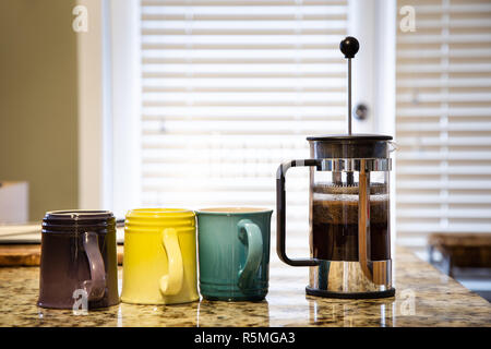 Eine französische Presse auf eine Küche Arbeitsplatte mit Kaffee brühen und bunten Tassen Kaffee Stockfoto