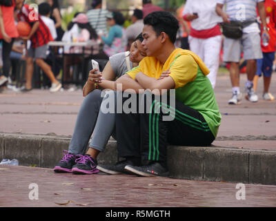 Horizontale Foto von Inhalt, jungen indonesischen teenage Mädchen ihren Kopf auf's Freund Schulter am Handy von selfies getroffen, die Tag. Stockfoto