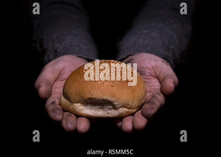 Armut Konzept. Die schmutzigen Hände Brot auf schwarzen Hintergrund. Stockfoto