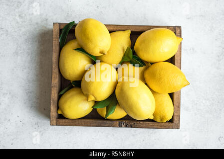 Zitronen mit grünen Blättern in Feld am weißen Stein Hintergrund, Ansicht von oben. Organische frische Zitrusfrüchte Zitronen. Stockfoto
