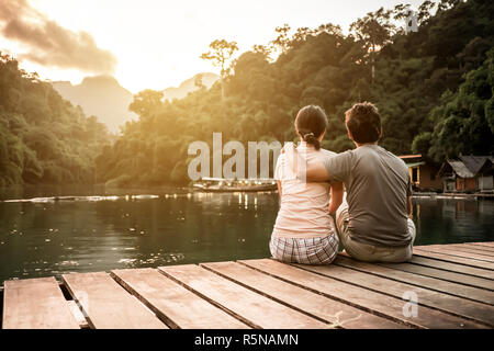 Paar verliebt sitzen auf die Holzbrücke und beobachten den Sonnenuntergang über die Berge und den See. Stockfoto