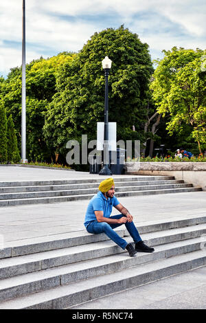 Junge indische Sikh sitzen auf der Treppe des Mount Royal Park und ein Gespräch mit seinen Kopfhörern in Montreal, Kanada. Stockfoto