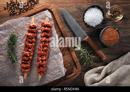 Raw türkischen Adana Kebab auf weißem kochen Papier und Holz Schneidebrett. Mit Kräutern, Gewürzen und kochmesser eingerichtet. Ansicht von oben. Stockfoto