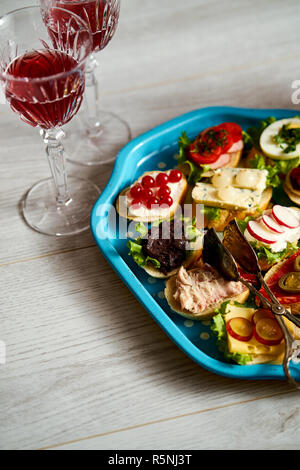 Set mini Sandwiches oder Tapas für Zwei mit Gläsern Wein auf hellem Holztisch Stockfoto