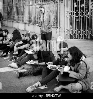 OAKLAND, CA - 6. Juni 2014: Millenials sitzen auf dem Bordstein essen Street Food zu einem monatlichen Art Gallery hop genannt Kunst Murmeln. Schwarze und weiße Quadrat. Stockfoto