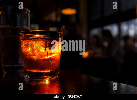 Cocktail in der Nähe auf einer Theke. Trinken ist gegen einen dunklen Hintergrund mit unscharfen Menschen beleuchtet. Stockfoto