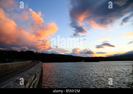 Ein bewölkter Sonnenuntergang über Marathon See in Kaletzi, in der Nähe von Marathon, Griechenland. Die Straße über den See ist direkt in der Damm gebaut. Stockfoto