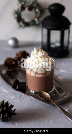Heiße Schokolade im Glas auf Metall Fach mit Löffel und schwarz Laterne in der Nähe auf grauen Hintergrund. Weihnachten Komposition. Stockfoto
