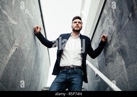 Junge stilvolle Geschäftsmann Mann mit Bart in einem modischen Anzug und Jeans. Modernes Bild der Jugend. Es steht auf dem Hintergrund von Marmor Wand Stockfoto