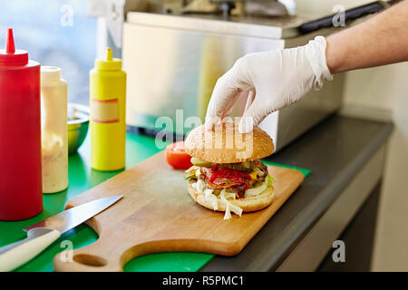 Behandschuhten Hand oben Bun auf einem großen leckeren Burger Stockfoto