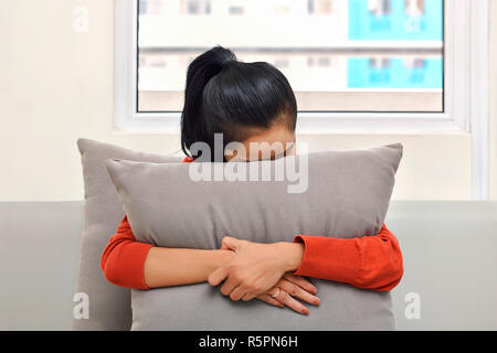 Junge asiatische Frau umarmen und versteckt sich hinter einem Kissen Stockfoto