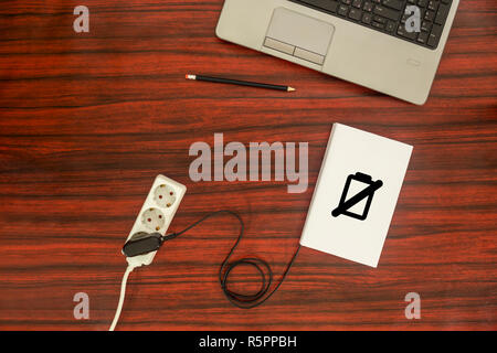 Oben Ansicht eines Buches an eine Steckerleiste über ein USB-Ladegerät angeschlossen ist. Das Batteriesymbol zeigt den Ladezustand. Stockfoto