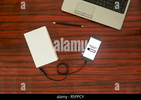 Oben Blick auf ein Buch, um ein BlackBerry-Smartphone über ein USB-Kabel auf dem Schreibtisch verbunden. Optische Zeichenerkennung laden Bar. Stockfoto