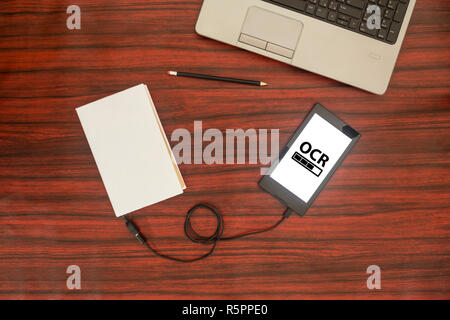 Oben Blick auf ein Buch, das zu einem Tablet-PC über ein USB-Kabel auf dem Schreibtisch verbunden. Optische Zeichenerkennung laden Bar. Stockfoto