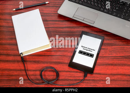 Buch zu einem Tablet-PC über ein USB-Kabel auf dem Schreibtisch verbunden. Optische Zeichenerkennung laden Bar. Stockfoto