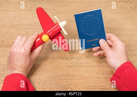 Männliche Hände halten ein Spielzeug Flugzeug und einem Pass über einen hölzernen Tisch Stockfoto