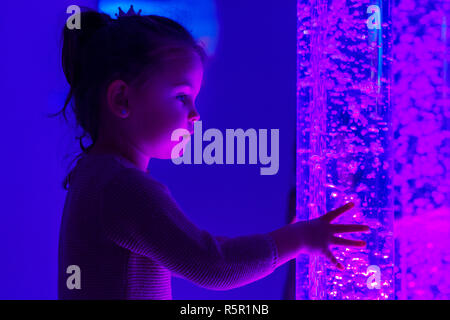 Kind in der Therapie sensorische Stimulation, snoezelen. Kind Interaktion mit farbigen Lichtern bubble Rohr Lampe während der therapiesitzung. Stockfoto