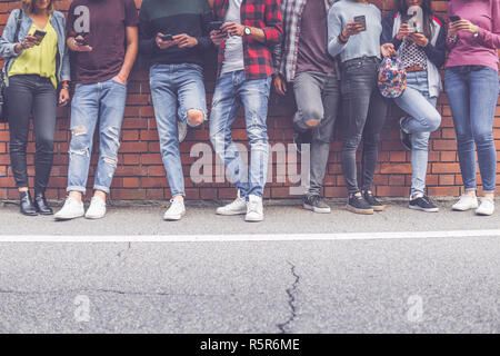 Gruppe der Acht jugendlich Freunde millenials Jungen und Mädchen beobachten Smart mobile Telefone vor der Mauer Hintergrund. Konzept der Jugend, Tech, soziale a Stockfoto