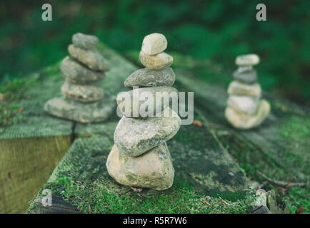 Kiesel Türme in einem Wald. Ausgewogene Steine in einem Stapel auf den hölzernen Hintergrund bedeckt mit Moos. Nahaufnahme von drei Stapel der Felsen Stockfoto