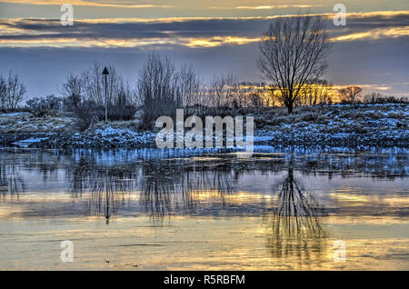 Bäume, Büsche, ein Navigationssystem, Mark, und verschneiten Ufer spiegeln sich in den ruhigen Gewässern der langsamen streaming IJssel in der Nähe von Zutphen, Niederlande du Stockfoto