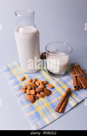 Vorderansicht. Natürliche Milch in Flaschen und Mandel Muttern und Zimtstangen auf Weiß und Blau serviette Hintergrund. Stockfoto