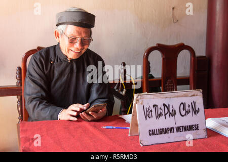 Hanoi, Vietnam - ca. Oktober 2015: kalligraph in Hanoi, Vietnam bietet seine Dienstleistungen und Handy zugleich. Stockfoto