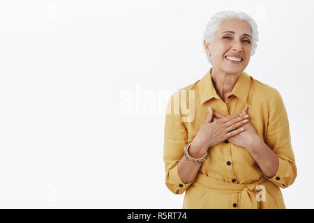 Ältere Frau immer Komplimente frisch und schön. Freut mich Glücklich charmante alte Dame mit weißen Haaren in stilvollen gelben Mantel Holding pa Stockfoto