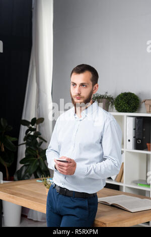 Thema Office Business. Hübscher junger kaukasischer Mann Selbstsicher und stark mit Bart in helles Zimmer auf Arbeitsplatz. stilvoll Hemd Stockfoto