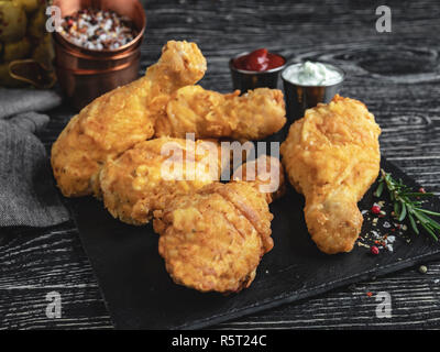 Fried Chicken Bein in Teig, roter und weißer Soße auf eine dunkle Oberfläche Stockfoto