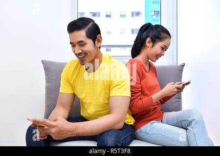 Jungen asiatischen Ehepaar auf dem Sofa sitzen mit Handy Stockfoto