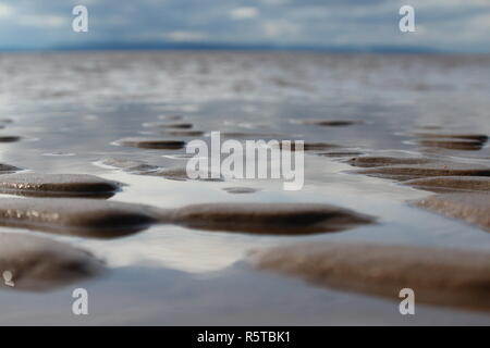 Eine niedrige Aufnahme von Wasser auf dem Sand, die den Himmel in der Findhorn, Schottland, Strand bei Flut ist out. Stockfoto