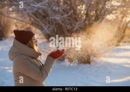 Winter Spaß, Urlaub, gutes Wetter und Personen Konzept - junge Frau in Rot winter Hut Schneegestöber von rot Handschuhe im sonnigen Wintertag. Stockfoto