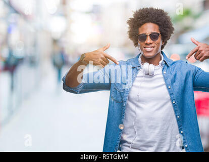 Afro-amerikanischer Mann mit Kopfhörern Musik hören über isolierte Hintergrund überzeugt mit einem Lächeln auf dem Gesicht, zeigen Sie sich selbst mit Fingern p Stockfoto