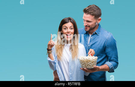 Junges Paar in Liebe essen Popcorn über isolierte Hintergrund mit einer Idee oder Frage Zeigefinger mit glücklichen Gesicht überrascht, Nummer eins Stockfoto