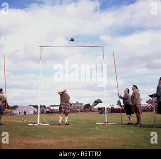 1960er Jahre, Highland Games, Schottland, Großbritannien. Bild zeigt einen Mitbewerber und der Beamten an das 'Gewicht über der Bar" Veranstaltung, die der Athlet das Werfen eines 56-pund (4-Stein) Gewicht mit angeschlossenen über einen horizontalen Balken mit einer Hand den Griff umfasst. Ein erfolgreiches Spiel wie hier gesehen ermöglicht die Wettbewerber in die nächste Runde in größerer Höhe zu gelangen. Stockfoto