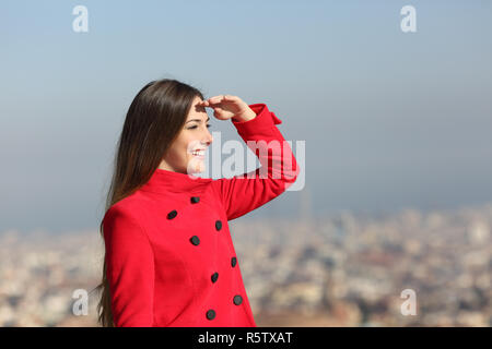 Gerne Frau in Rot Scouting mit der Hand auf der Stirn im Winter mit städtischen Hintergrund Stockfoto