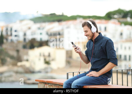 Glückliche Menschen mit Kopfhörern hören die Musik auf einem Felsvorsprung mit einer Stadt im Hintergrund Stockfoto