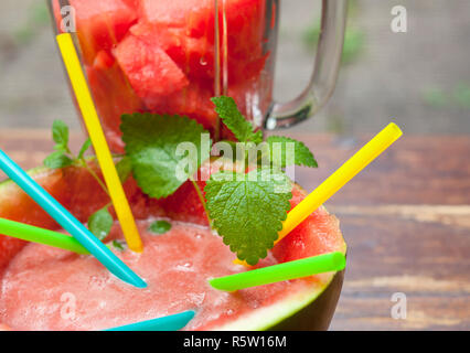 Halbe Wassermelone mit Wassermelone Saft und Strohhalme auf Garten Hintergrund Stockfoto