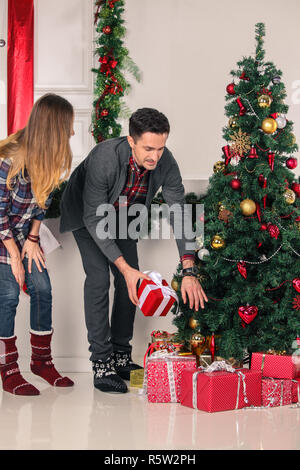 Glückliche Eltern, Weihnachtsgeschenke für die Kinder unter dem geschmückten Baum Stockfoto