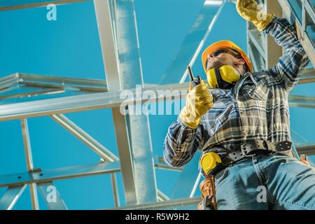 Bauarbeiter im Einsatz. Kaukasische Auftragnehmer mit Walkie Talkie und das Skelett aus Stahl Projekt. Industrial Site. Stockfoto