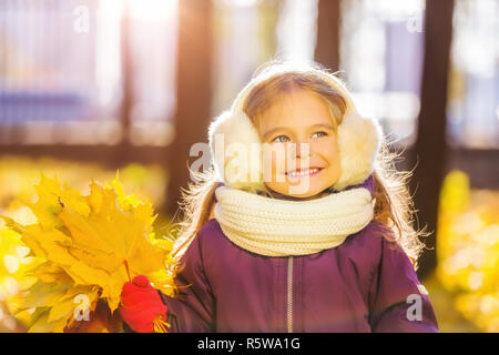 Glückliches kleine Mädchen in Ohrenklappen mit Herbst Blätter Stockfoto