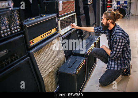 Junge hipster sitzen vor der Sound Controller und sie berühren. Kerl sitzt auf einem Knie Stockfoto