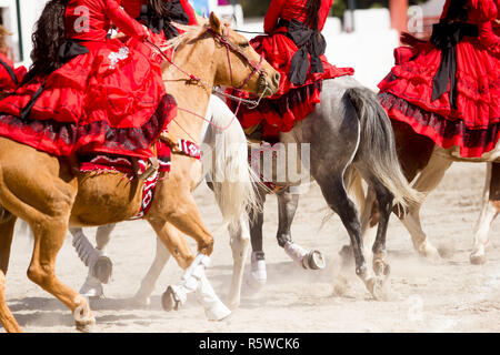 Fahrt Gruppe von mexikanischen escaramuza Mädchen mit roten mexikanischen Kleider reiten auf einem Rodeo Stockfoto